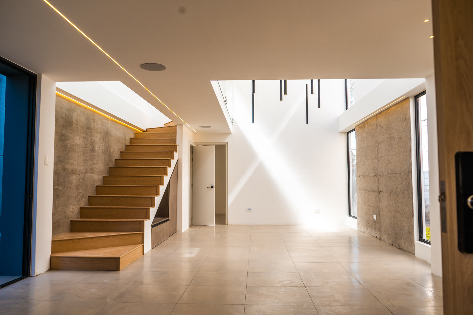 Sala de doble altura con escalera de madera y muro de hormigón visto